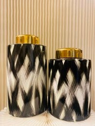 Tall, cylindrical ceramic vase with a black and white diamond pattern and gold-colored lid.