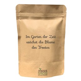 A tall, round sunflower grows in the garden of time, with a natural, earthy color palette. The product packaging features the German text "Im Garten der Zeit wächst die Blume des Trostes" which translates to "In the garden of time grows the flower of solace".