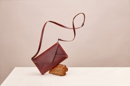 Rectangular leather clutch with a long strap in a deep red color.