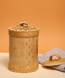 Cylindrical cereal storage jar with wooden lid, made of natural materials with a rustic, textured appearance.