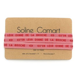 A pair of red shoelaces with the text "Soline Camart" and "Leur donne de la brioche" printed on them. The shoelaces appear to be made of a soft, flexible material.