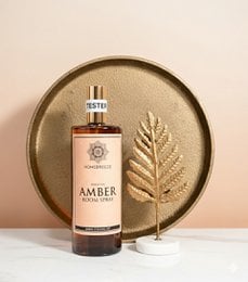 A floral, fragrant room spray in a glass bottle with a gold cap and label. The spray is described as "Original Pink Orchid" and is 250 ml in size. The image shows the bottle on a round wooden surface with some natural elements like leaves.