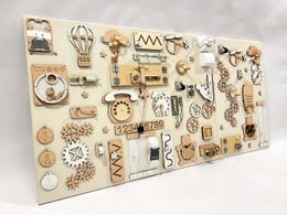 A large wall activity panel with various sensory elements for toddlers, including beige and ocean blue color variants.
