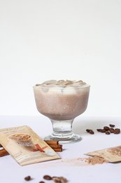 Instant Turkish coffee drink in a glass with coffee beans and cinnamon sticks.