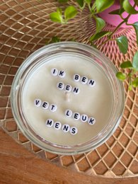  A round, tall candle in a glass jar with a rose quartz gemstone. The candle is scented with essential oils and has a hidden message that says "I am a cool fun person".