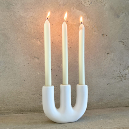  A white, modern candelabra with three tall, cylindrical candle holders. The candelabra has a simple, minimalist design and is made of a smooth, matte material.