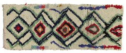 This image appears to be a handwoven area rug or carpet with a geometric diamond pattern in shades of beige, blue, and red. The rug has a textured, woven appearance and the pattern creates a visually striking and intricate design.