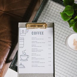 A metal clipboard with a green finish, featuring a coffee menu with various coffee options and prices.