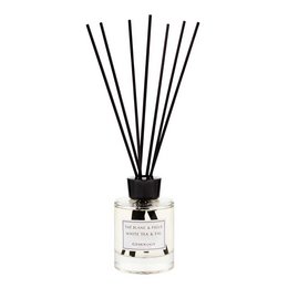 A clear glass reed diffuser bottle with black reed sticks, containing a white liquid fragrance. The diffuser is accompanied by a natural stone or crystal.