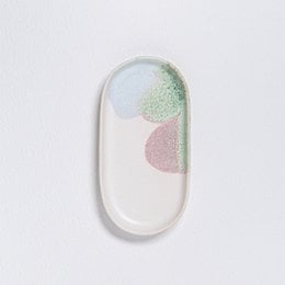 Oval-shaped white ceramic jewelry tray with pastel-colored abstract shapes.