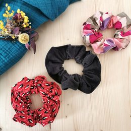 Colorful, patterned scrunchies in various shapes and styles, including a round, floral-patterned scrunchie and a black scrunchie.