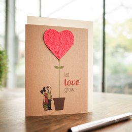 Greeting card with a red heart-shaped flower and a person watering it, with the text "let love grow" on a kraft paper background.