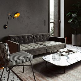  A modern, tufted gray sofa with a glass-topped coffee table and a black and white patterned armchair in a minimalist living room setting.