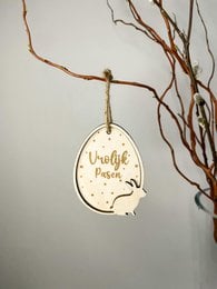 Oval-shaped wooden Easter pendant with "Happy Easter" text and a hare silhouette design. Hanging from a branch with twigs.