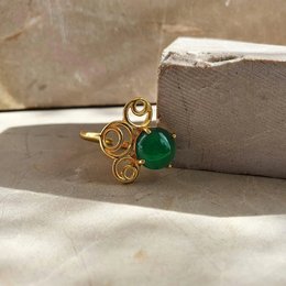 A gold-toned statement ring with a round green gemstone at the center, surrounded by a swirling abstract design.
