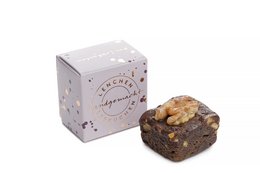 A square-shaped gingerbread cake in a decorative box with a floral pattern. The cake appears to be a rich, dark brown color with visible chunks of nuts or other ingredients.