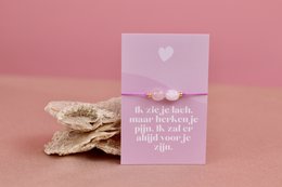  Beaded bracelet in neutral tones with a heart-shaped charm and a motivational message on a pink background.

The image shows a beaded bracelet in neutral tones, such as tan and white. The bracelet has a heart-shaped charm attached to it. The bracelet is placed on a pink background, along with a small card or note that displays a motivational message.