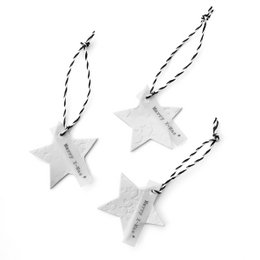 White porcelain star-shaped ornaments with a textured diamond pattern on a gift-wrapped box with pine branches.