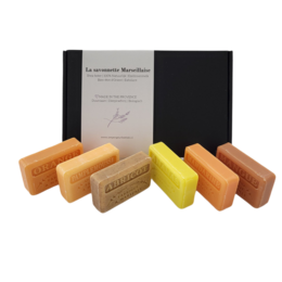 A set of colorful, artisanal soap bars in various citrus scents including pineapple, mandarin, apricot, grapefruit, mango, and orange. The soap bars are presented in a gift box.