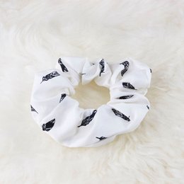 White scrunchie with black feather print, made of soft, stretchy fabric.