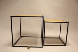 A set of two modern, minimalist side tables with a black metal frame and a yellow woven rattan top. The tables have a simple, geometric design and are suitable for use as end tables or nightstands in a living room or bedroom.