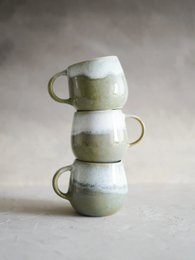  Stacked ceramic mugs in a muted green color with a simple, minimalist design.
