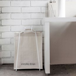 A white paper bag holder with the text "everyday design" printed on it. The bag holder has a simple, minimalist design and appears to be made of sturdy materials.