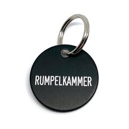 Black round key fob with silver text "RUMPELKAMMER" printed on it. Metal ring for attaching to keys.