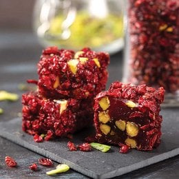 Fruit-flavored gummy cubes with a vibrant red color and visible pieces of fruit or nuts. The cubes have a soft, chewy texture and appear to be garnished with pistachio nuts or other green garnishes.
