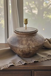  A rustic ceramic table lamp with an earthy, textured finish. The lamp has a rounded, bulbous shape and a brass-colored lamp base.