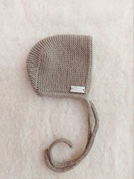 Soft, cozy merino wool bonnet in a neutral beige color. Features a simple, minimalist design with a small metal snap closure. Ideal for keeping baby's head warm during the cooler months.