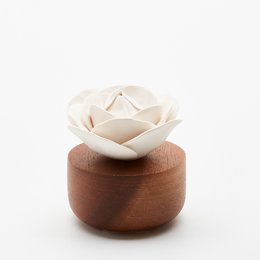 White ceramic rose-shaped diffuser on a wooden base, with a small glass bottle of fragrance oil.