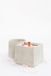 Oval and quadrat-shaped pillar candle in a neutral concrete color. The candle has a simple, minimalist design that would complement a variety of home decor styles.