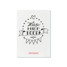 A white greeting card with the text "Hiep hiep hoera" (Dutch for "Hip hip hooray") and a decorative banner with hearts and stars.