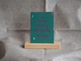 A green greeting card with the text "A very merry christmas to you" written in cursive font. The card has a simple, minimalist design with a few small decorative elements like snowflakes.