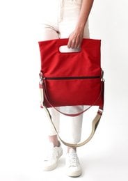Red canvas tote bag with zipper closure and leather trim. Rectangular shape, suitable for everyday use.