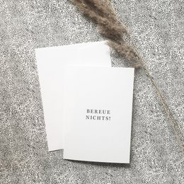 A folded card with the text "Bereue nichts!" (Don't regret anything) printed on it.