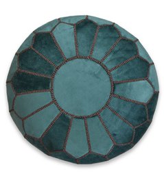  A round, green velvet pouffe with a geometric pattern resembling a flower or sunburst design. The pouffe appears to be stuffed and ready for use as a footstool or extra seating.