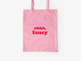 A pink cotton tote bag with the text "uhhh, fancy" printed in red on the front.
