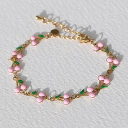 A delicate gold-toned bracelet with pink and white floral accents, featuring a charm and tassel detail.