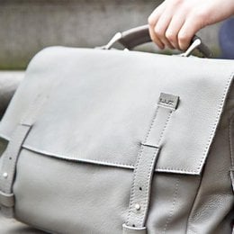 Gray leather satchel bag with adjustable strap and flap closure.