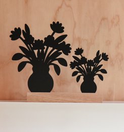 Wooden flower pots with black silhouette designs, featuring a tall pot and a shorter pot. The pots appear to contain decorative flowers or plants.