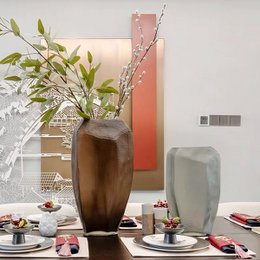 A tall, brown glass vase with a unique, angular shape. The vase features a rich, chocolate-brown color and a sleek, modern design that would complement a variety of home decor styles.