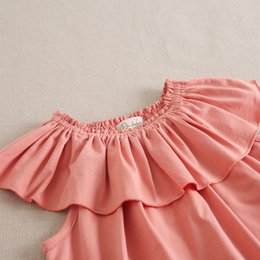  Girls' flowing coral pink t-shirt with ruffled neckline, available in sizes 3 to 12 years.