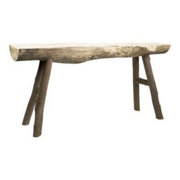 A rustic wooden bench with a natural, unfinished appearance. The bench features a long, rectangular seat made from a single piece of wood with a rough, textured surface. The legs are simple, wooden supports that provide a sturdy base for the bench.