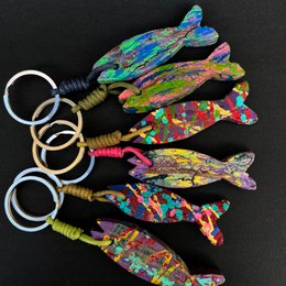 Colorful, abstract fish-shaped keychains with vibrant, splattered paint patterns. The keychains feature a variety of shapes and sizes, including tall, round, and elongated fish designs.