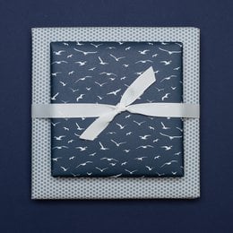 Petrol blue wrapping paper with a double-sided design featuring a repeating pattern of white birds or feathers. The wrapping paper has a polka dot border and is tied with a blue ribbon.