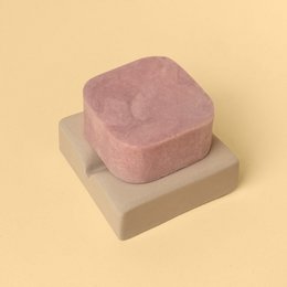  Small, square soap dish in light pink and beige colors. Made of ceramic material with a minimalist, geometric design.