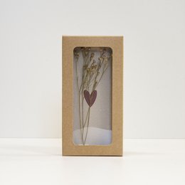 A small, rectangular box containing a dried flower arrangement with a heart-shaped accent. The box is made of a natural, earthy material, likely cardboard or wood, and the dried flowers inside are delicate and minimalist in design.