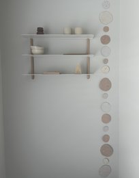 Decorative paper garland with neutral-colored circles, displayed on a white wall with a wooden shelf and decor items.